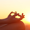 cropped image of hands in yoga pose with sunset in background