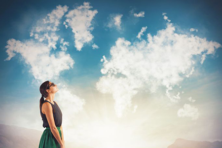 woman with suitcase ooking at clouds - shaped like world map