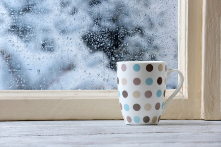 Cup of hot drink by cold and wet window