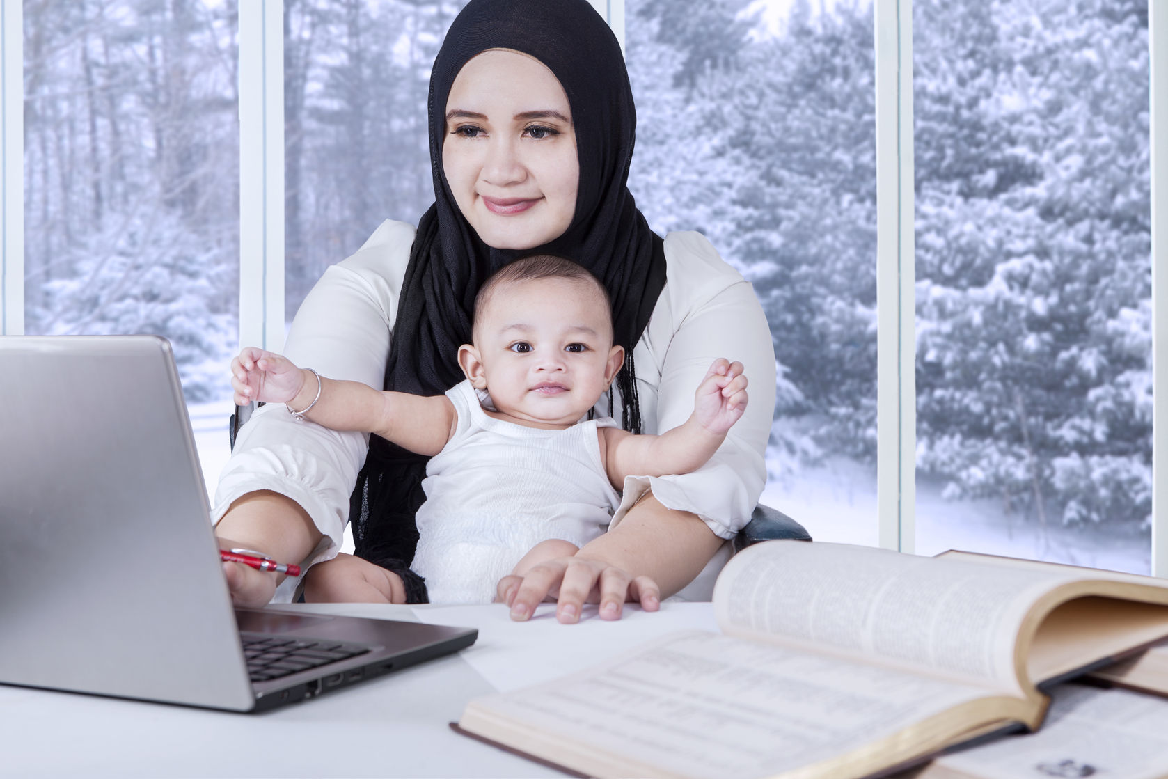 Woman wearing a hijab with a baby on lap sitting on a computer. 