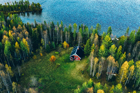 Aerial top view of red log cabin or cottage with sauna in spring forest by the lake in rural Finland