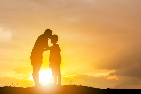 Silhouette of a mother kissing his son in a forehead on the sunset summer day.