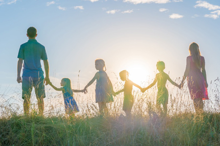 A large family is standing holding hands against the background of the sunset.