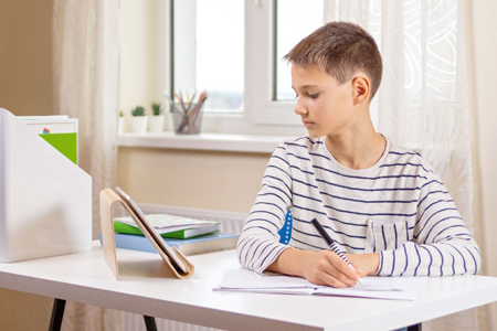 Kid with digital tablet computer writing, doing homework at white desk. Online learning, remote educ
