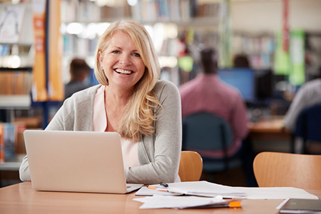 mature woman sitting in library with laptop and books