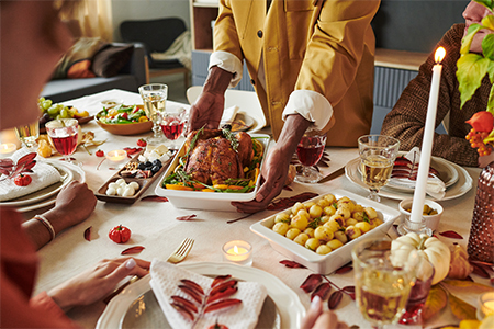 Hands of a person serving roasted turkey to diverse group of adults sitting around Thanksgiving dinn