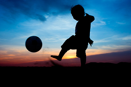 silhouette of boy kicking ball