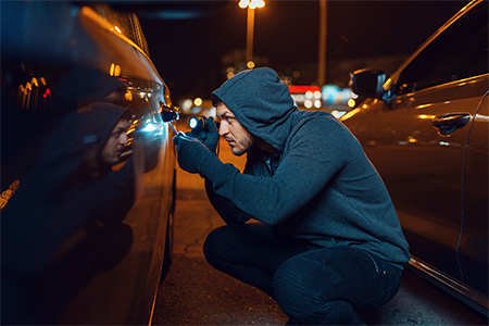 Car thief with screwdriver breaking door lock. Hooded male robber opening vehicle on parking