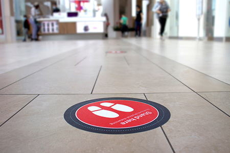 A red sticker in a Canadian Mall warning to stand here to respect covid-19 distancing rules.