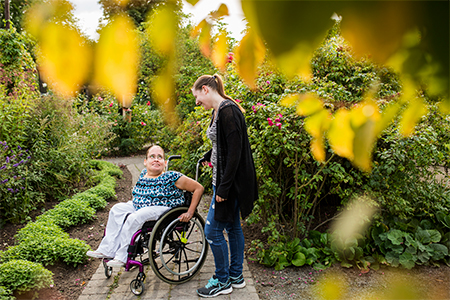 Disabled woman in wheelchair with assistant in garden