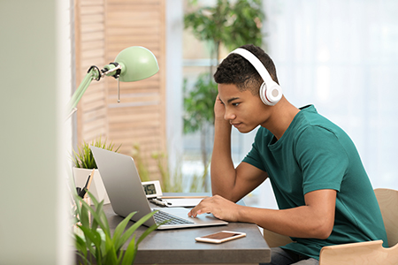 African-american teenage boy with headphones using laptop at table in room