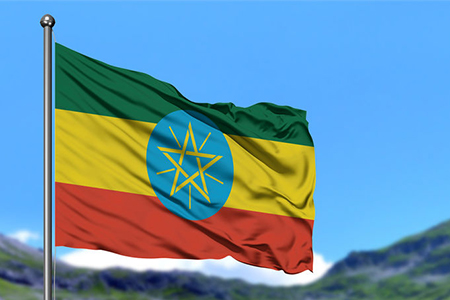 Ethiopia flag waving in the blue sky with green fields at mountain peak background. Nature theme.