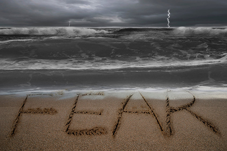 Fear written in sand on beach - stormy cloud and waters 
