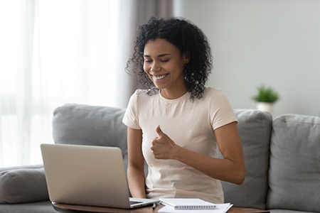 Woman smiling, giving thumbs up to laptop