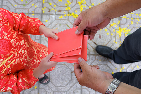 man handing red envelope to woman - top, cropped view of hands only