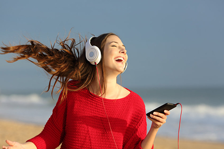 Happy girl wearing red colorful jersey dancing singing and listening music on line with headphones f