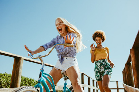 Excited girl cycling on a boardwalk with her friends running. two woman friends enjoying themselves 