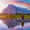 Couple adventurous friends are canoeing in a lake surrounded by the Canadian Mountains. Colorful Sun