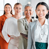 Portrait of smiling businesswomen standing in office with colleagues in background