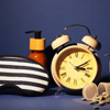Sleeping mask, alarm clock, cosmetic bottles and pills on color background