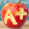A+ carved into apple in front of chalkboard