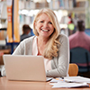mature woman sitting in library with laptop and books