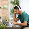 African-american teenage boy with headphones using laptop at table in room