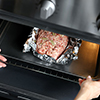 Woman putting baking tray with raw turkey meatloaf into oven