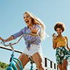 Excited girl cycling on a boardwalk with her friends running. two woman friends enjoying themselves 
