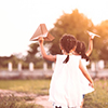 Back view of two asian child girls running and playing toy paper airplane together in the field in v