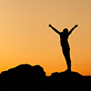 Stock Photo - Silhouette of happy young woman with arms raised up against beautiful colorful sky. Su
