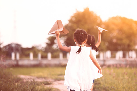 Back view of two asian child girls running and playing toy paper airplane together in the field in v