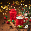 Red cup of hot cocoa with marshmallows and candy canes on wooden table with christmas tree