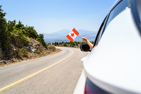 holding Canada flag from the open car window driving along the serpentine road in the mountains