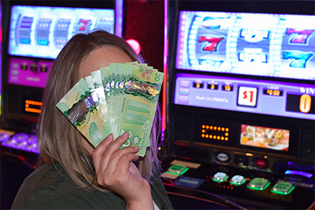 Woman covering her face with Canadian cash money in casino beside slot machines