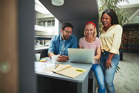 Diverse group of laughing businesspeople working on a laptop together in a meeting pod