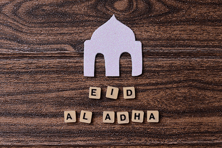Eid Al Adha word with mosque ornament on wooden background for islamic festive celebration