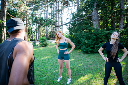Three people are exercising in a park, personal trainer is holding a class with his athletes