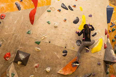 Sporty little girl climbing artificial boulder on practical wall in gym