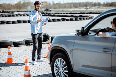 Male instructor teaching young woman driver to park a car on the training ground