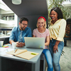 Diverse group of laughing businesspeople working on a laptop together in a meeting pod