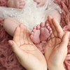 Mother holding the feet of a newborn baby on a background of pink flokati