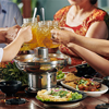 Hands of family members toasting with glass mugs over dinner table with hotpot