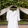 A white wedding dress hangs off the side of a beautiful ceremony arch