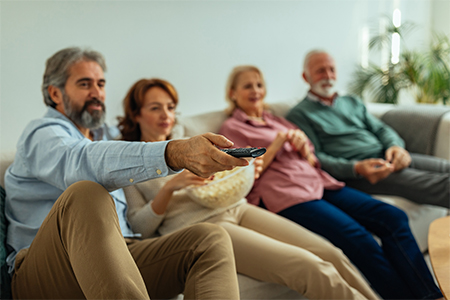 Four of senior friends siting on the couch in the living room and watching tv