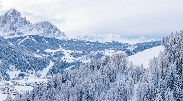 Photo of lit up cabin in the winter. Snowy mountains seen in the back.