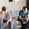 Two stressed multi ethnic men with mask as friends looking depressed while video calling at home und