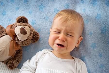 One year old baby lying in bed holding a plush teddy bear