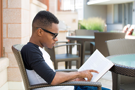  young man with big black glasses, sitting down and reading, isolated outdoors background