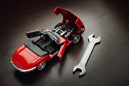 Model of red cabriolet with opened doors and hood and wrench on wooden surface
